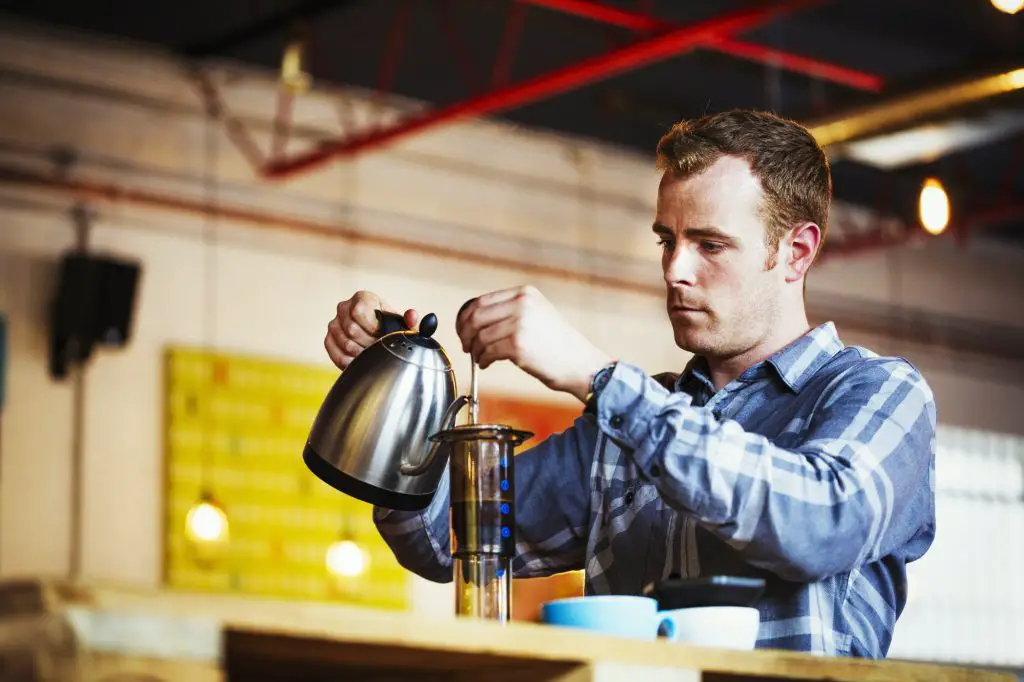 Specialist coffee shop. A man pouring hot water into a coffee perculator.