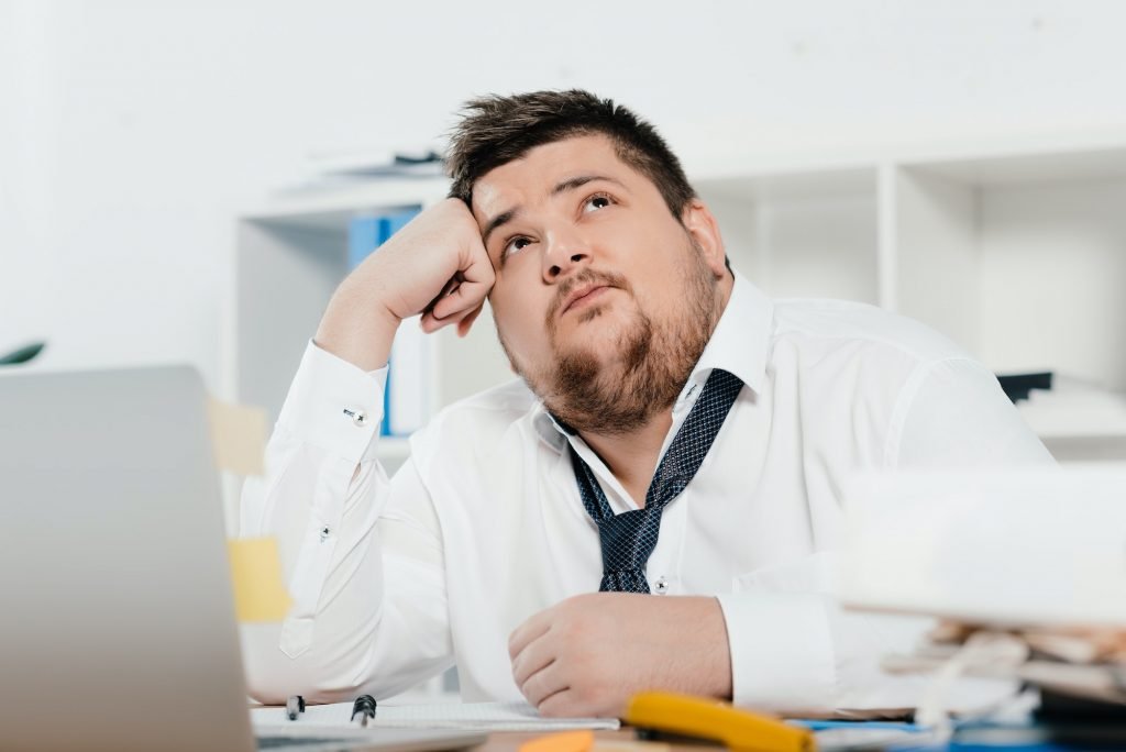 thoughtful fat businessman with laptop at workplace in office