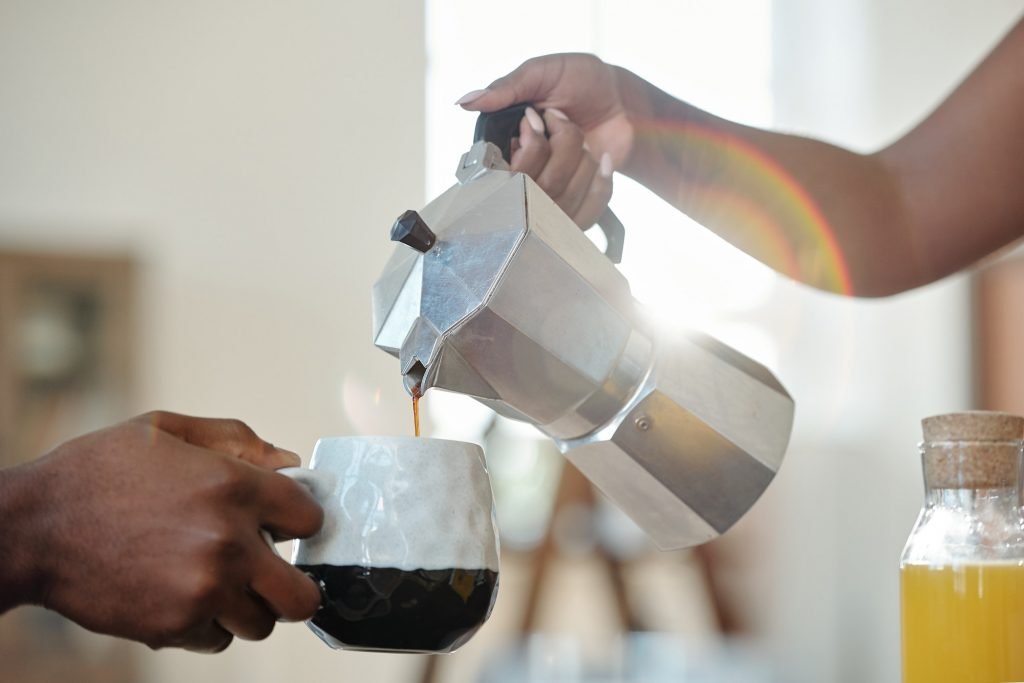 Hand of young African female pouring coffee or tea into mug of her husband