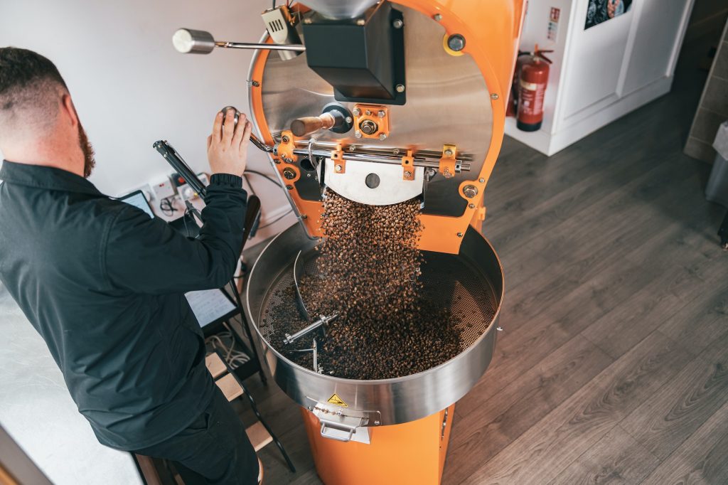Barista pouring freshly roasted coffee beans from large coffee roaster into cooling cylinder