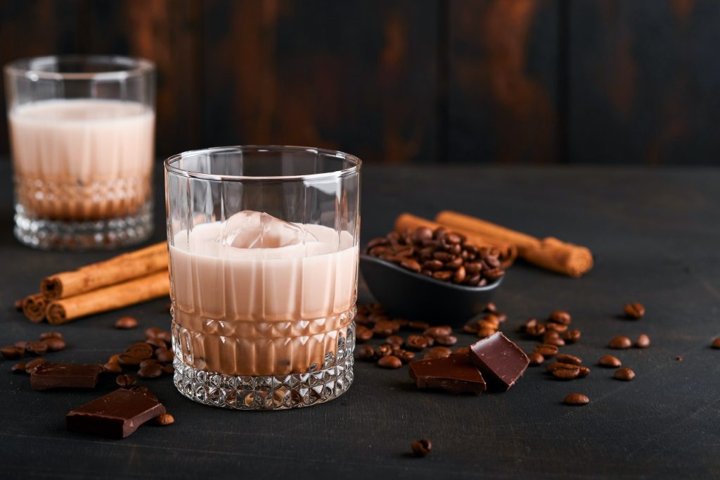 Glass of Irish cream baileys liqueur with roasted coffee beans, cinnamon and chocolate on dark wood