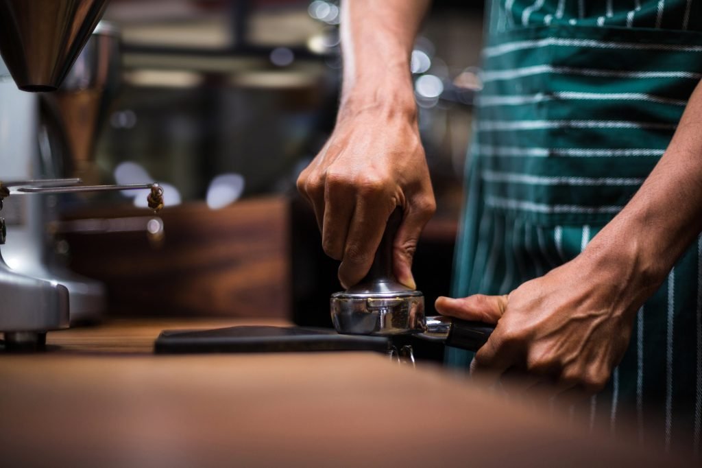 Waiter squeezing the coffee in the percolator at the coffee shop